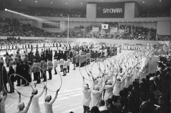 Athletes and officials in the Makomanai indoor skating rink for the closing ceremony of the Sapporo Winter Olympic Games in 1972. The words “Denver, 1976,” can be seen on the electric sign board.