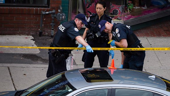 Police investigate a car with a bullet hole within the scene of the shooting.