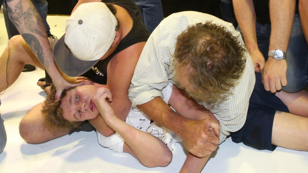 Supporters hold down an activist after he smashed an egg on the head of Fraser Anning.