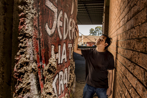 Raymond Chim with the section of the Berlin Wall that sat unknown in a Blacktown warehouse. The side that faced west Germany has graffiti reading 'Everyone is powerful'.