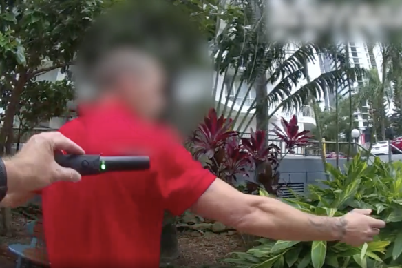 Queensland police officers search a man with a metal-detection wand.