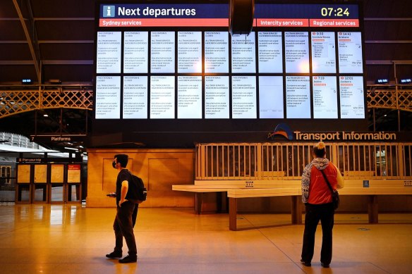 Commuters at Central Station stand in front of the departures board displaying a notice that all train services are suspended.