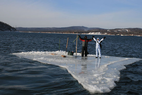 Two fishermen use a smaller piece of ice as a raft and try to row to land.