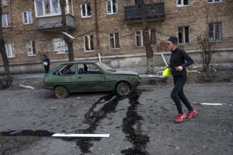 A woman exercises near a car and apartments damaged by shelling, in Kyiv, Ukraine.
