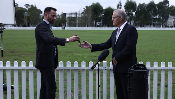 PM Scott Morrison is handed a phone by a media adviser.