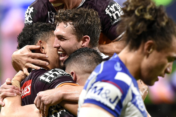 Xavier Coates is mobbed by his Broncos teammates after scoring a try.