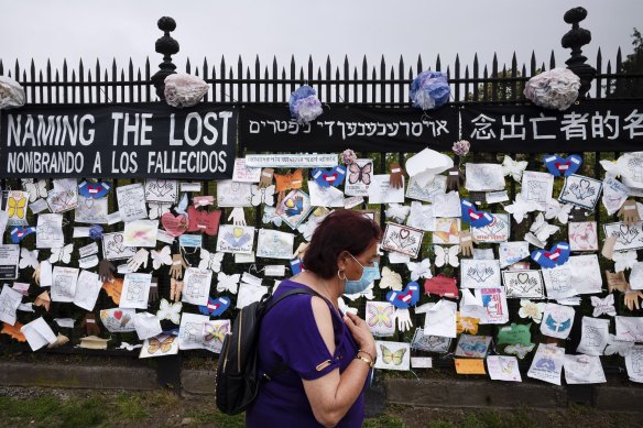 A woman passes a fence decorated with tributes to COVID-19 victims outside Brooklyn's Green-Wood Cemetery in New York.