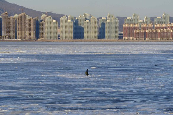 A fisherman walks on the partially frozen Jinzhou Bay of the Bohai Sea near residential construction sites in Dalian, Liaoning province.
