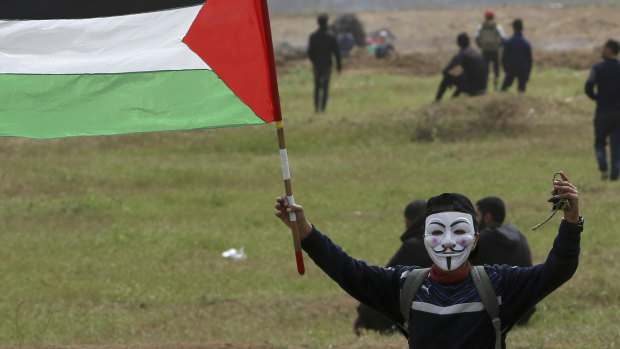 A masked protester waves his national flag near the fence of the Gaza Strip border with Israel, marking the first anniversary of Gaza border protests east of Gaza City on Saturday, March 30.