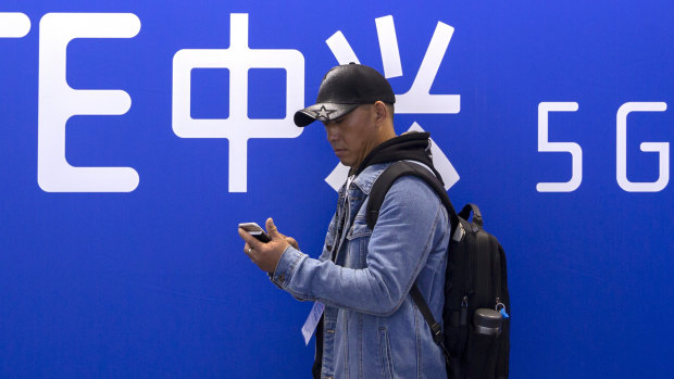 A man uses his smartphone near a display for 5G services from Chinese technology firm ZTE. China officially launched its 5G network on Friday.