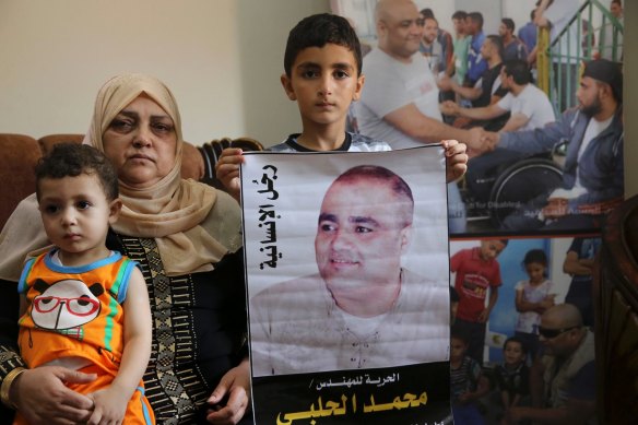 Amal el-Halabi, 57, holds her grandson Fares, 18 months, while another grandson Amro, 7, holds a picture of his father Mohammed el-Halabi, at the family home in Gaza City.  The Arabic on the picture reads: “The man of humanity”.