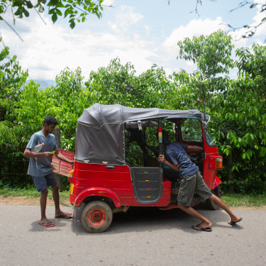Young men push a stalled tuk-tuk on a road through a cinnamon plantation in Kuruwita. 