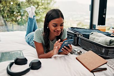 a woman lying on her bed on her phone with a half-packed suitcase