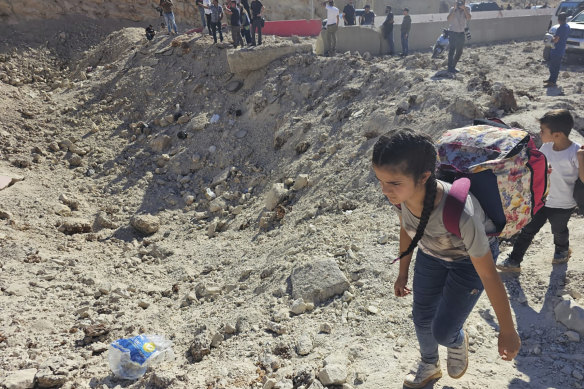 A girl carries her belongings crossing on foot into Syria through a crater caused by an Israeli airstrike to cut the road between the Lebanese and the Syrian checkpoints, at the Masnaa crossing, in the eastern Bekaa Valley.