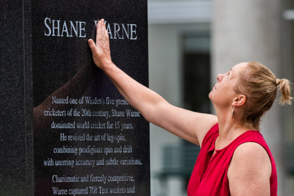 A woman leaves flowers at Shane Warne’s statue outside the MCG on Saturday morning.