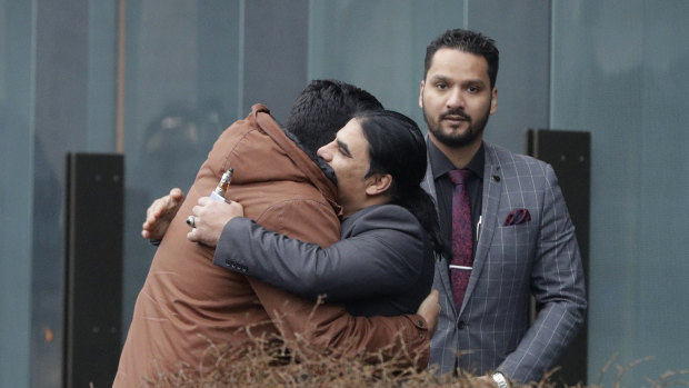 Abdul Aziz, center, a survivor of the Linwood mosque shootings, is embraced by friends outside the Christchurch District Court.