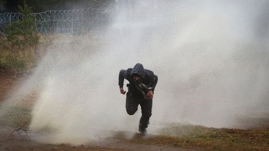 A man runs away from a water cannon during clashes between migrants and Polish border guards at the Belarus-Poland border on Tuesday.