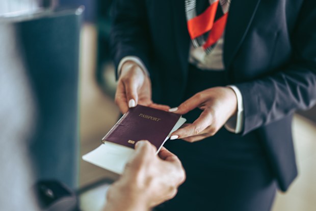 Closeup of flight attendant taking passport of tourist at airport check-in counter. 