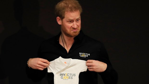 Prince Harry holds up an outfit for his newborn son presented by Princess Margriet of the Netherlands.