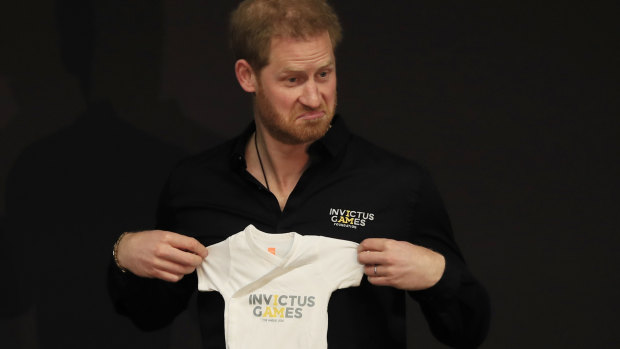 Prince Harry holds up an outfit for his newborn son presented by Princess Margriet of the Netherlands.