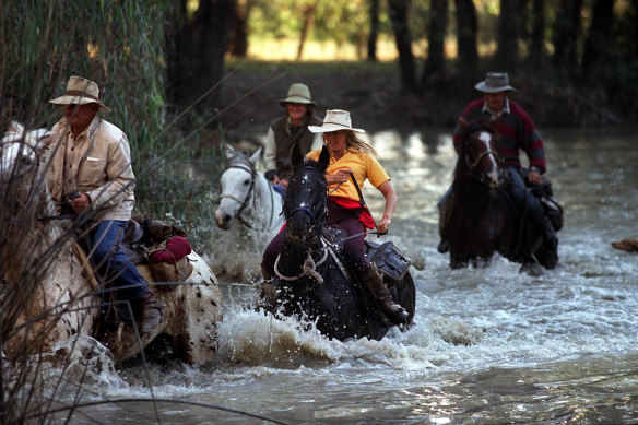 Horse riders cross a river during a muster.