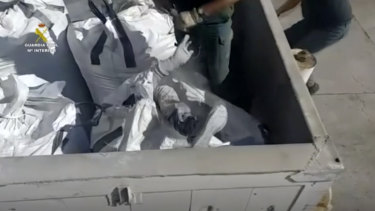 Disponible por la Compañía de la Guardia Civil, un oficial de la Guardia Civil asiste a un hombre con una bolsa gris en un contenedor en Melilla, España.
