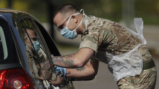 A National Health Service worker is tested by a soldier at a drive-through testing centre in a car park at Chessington World of Adventures near London.