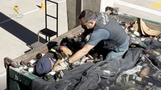 An officer helps a man out from under glass bottles in a container in Melilla, Spain.