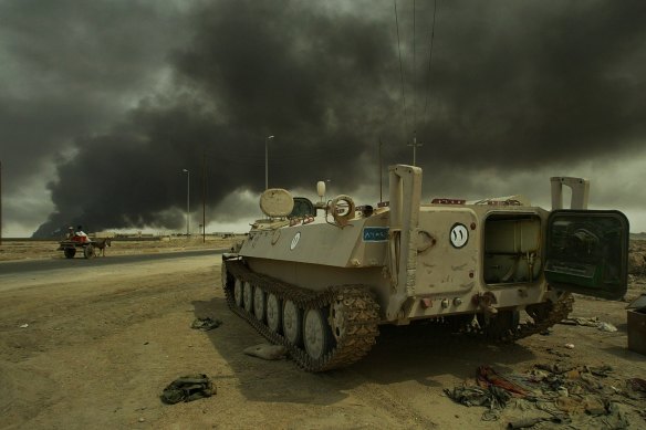 Smoke from oil fires fill the sky as a man and child ride their donkey-pulled cart past an abandoned Iraqi armoured personnel carrier on the road to Basra, during the first days of the invasion of Iraq in March, 2003.