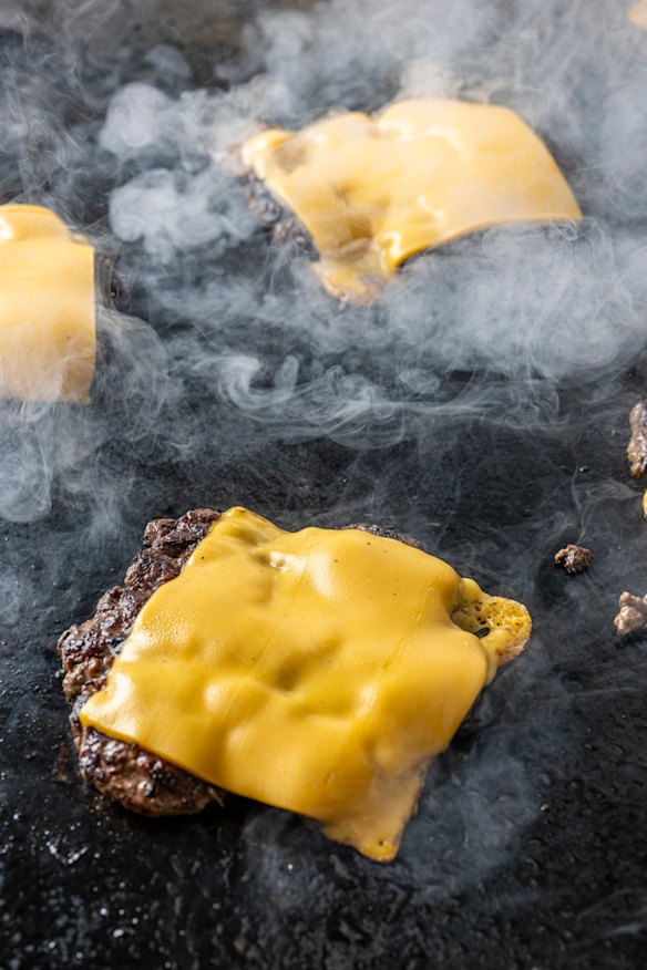 Burgers are cooked smash-style on the grill. 
