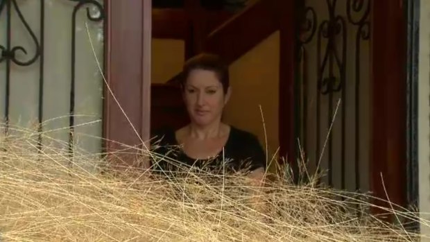 A resident of a Melbourne housing estate surveys her yard which has been engulfed by tumbleweeds.