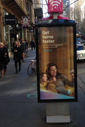A Telstra telephone booth in Melbourne's Collins Street with an advertising display sign tacked on the side.