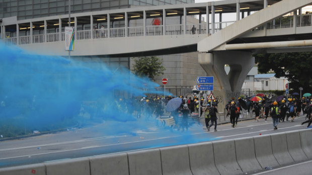 A police vehicle sprays blue-coloured water at anti-government protesters.
