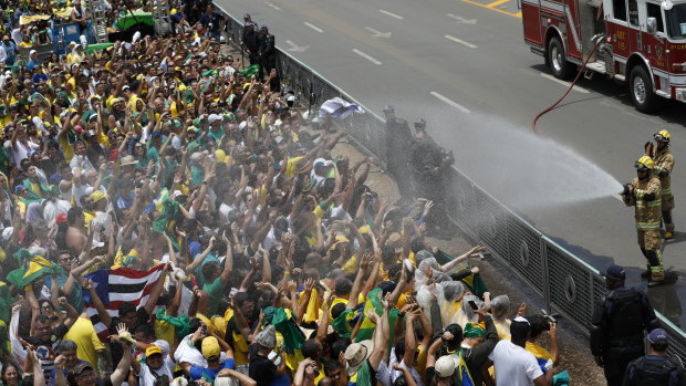 Supporters of Brazil's President Elect Jair Bolsonaro are cooled down with a water hose by firefighters.