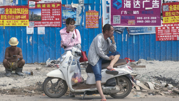 People wait in front of advertisements in Chinese pasted on a fence outside a construction site in Sihanoukville, Cambodia.