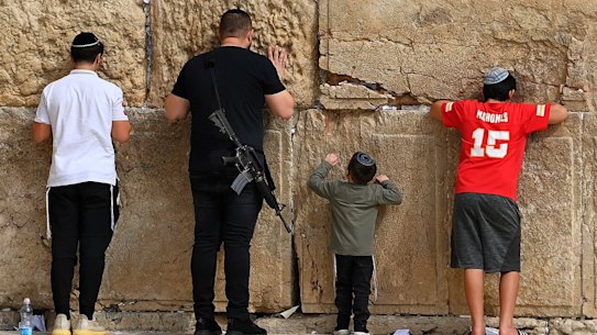An armed man prays with his son, second from right, at the Western Wall in the old city of Jerusalem.