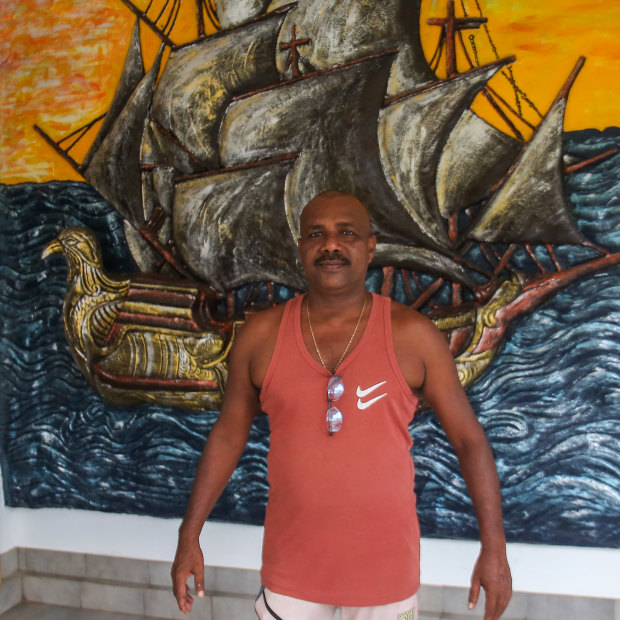 Fernando poses for a photo outside his house, which has a large mural of a ship next to the front door.