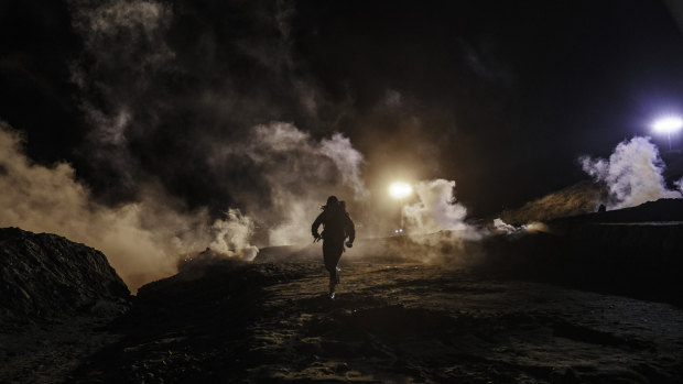 Migrants run as tear gas from US Border Protection officers is shot to the Mexican side of the border fence.