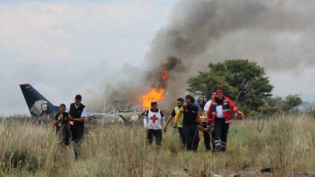 Airline workers, left, walk away from the site where an Aeromexico airliner crashed in a field near the airport in Durango, Mexico.
