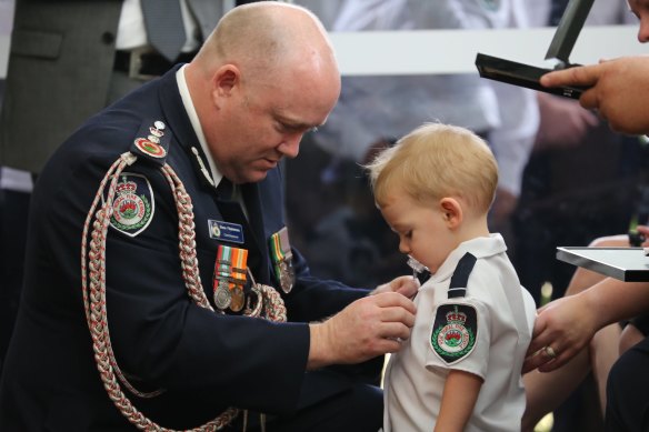 RFS Commissioner Shane Fitzsimmons pins the posthumous service medal of Geoffrey Keaton onto his son, Harvey. Geoffrey died fighting bushfires in December.