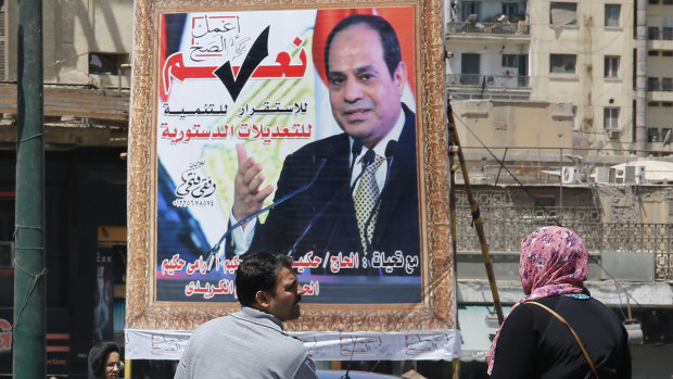 People walk past a banner supporting proposed amendments to the Egyptian constitution with a poster of Egyptian President Abdel-Fattah el-Sisi in Cairo.