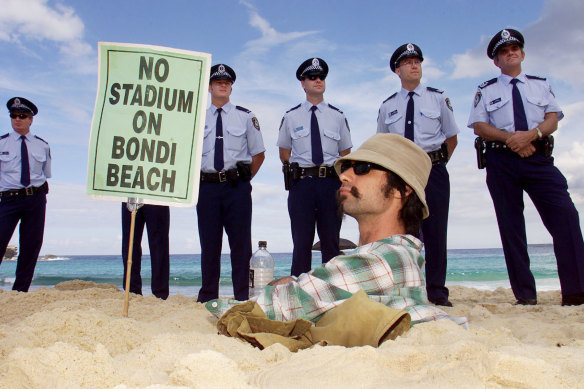 A protestor does his best to halt construction as police look on, slightly bemused.