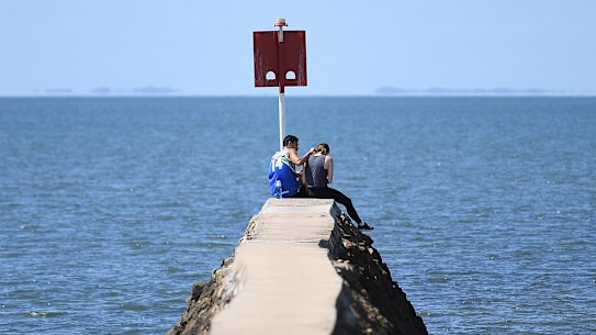 A teenage couple sit at the end of a sea wall at the Wynnum foreshore in Brisbane, Monday, April 6, 2020. Queensland has seen a reduction in new coronavirus cases as people are urged to stay at home and practice social distancing. (AAP Image/Dan Peled) NO ARCHIVING   
