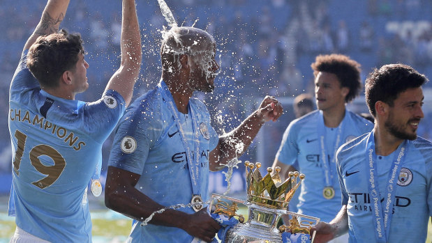 City's John Stone pours champagne over teammate Vincent Kompany, holding the Premier League trophy.