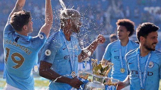 City's John Stone pours champagne over teammate Vincent Kompany, holding the Premier League trophy.