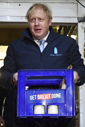 Britain's Prime Minister Boris Johnson carries a crate of milk bearing the Conservative Party slogan.