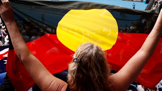 A spectator holds up the Indigenous flag as Ash Barty wins her third-round match at the Australian Open in January.