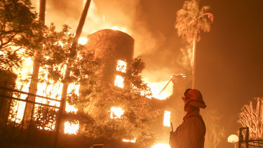 A firefighter keeps watch as the Woolsey Fire burns a home in Malibu, California.