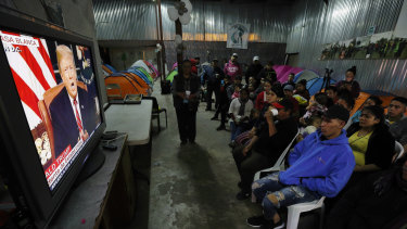 Migrants mainly from Mexico and Central America look on as US President Donald Trump gives his prime-time address about border security, watching from a border migrant shelter in Tijuana, Mexico. 