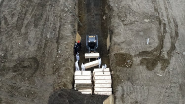 Workers wearing personal protective equipment bury bodies in a trench on Hart Island in the Bronx borough of New York on Thursday.